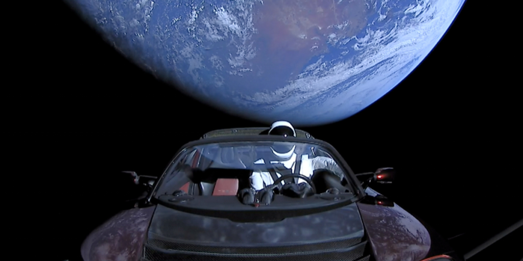 Tesla roadster in space with spaceman behind wheel. Earth in background.