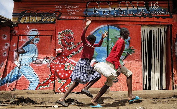 Two children run past a painted mural warning about COVID-19 in Nairobi.